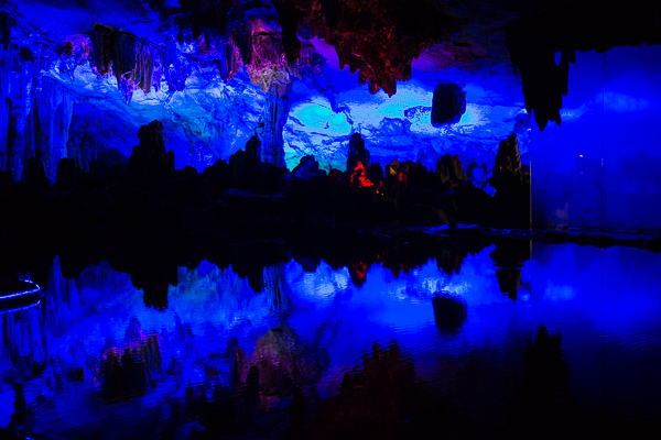 Formations lit by colored lights with their reflection in water in the Reed Flute Cave.